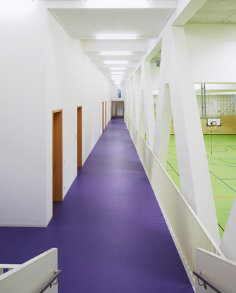 Neubau Sporthalle der Grundschule Rebstock: Innenperspektive, Weg zu den Umkleiden, Boden in Violett, daneben Hallenboden in Grün